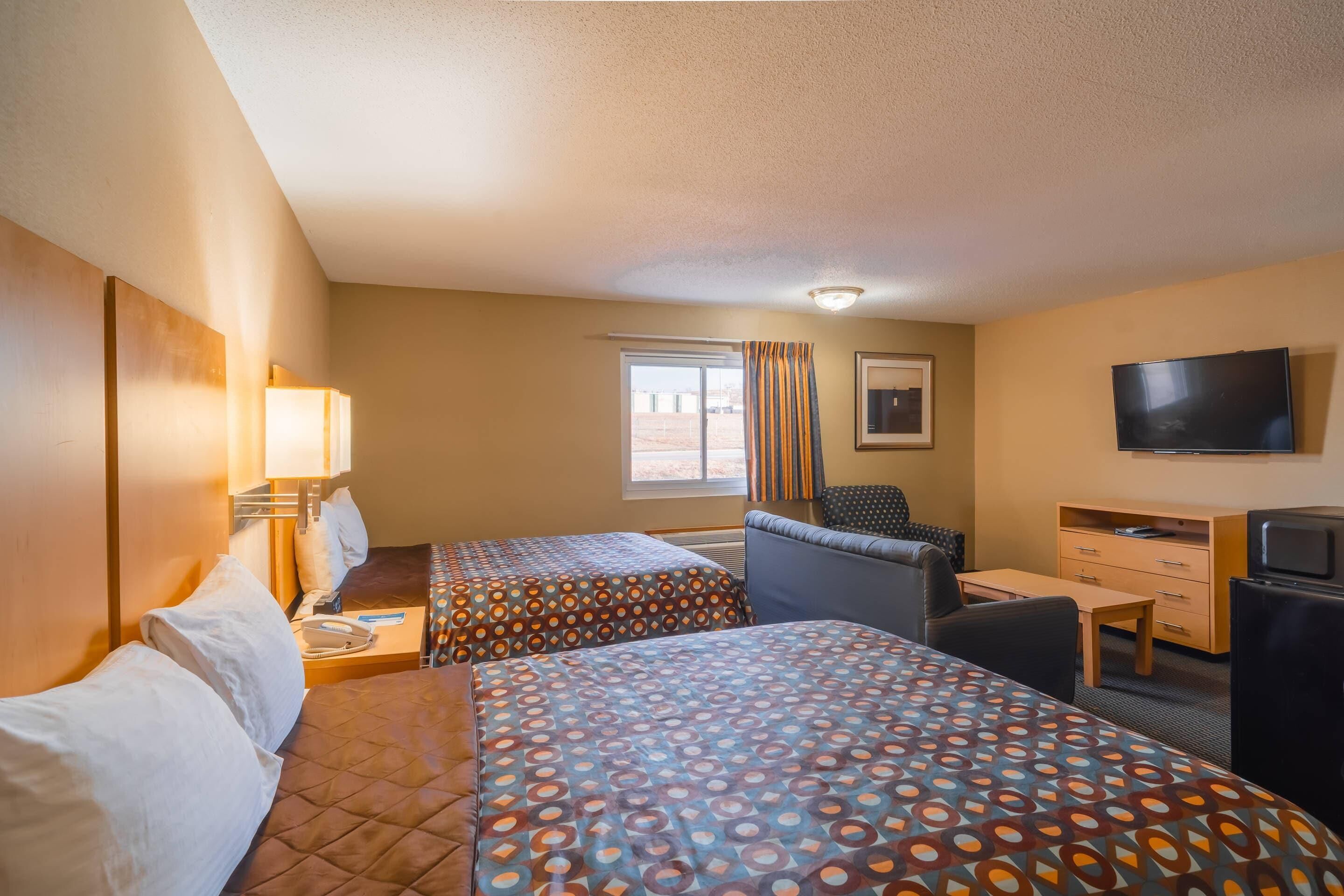 A hotel room with two beds, a desk, a chair, a television, and a window.