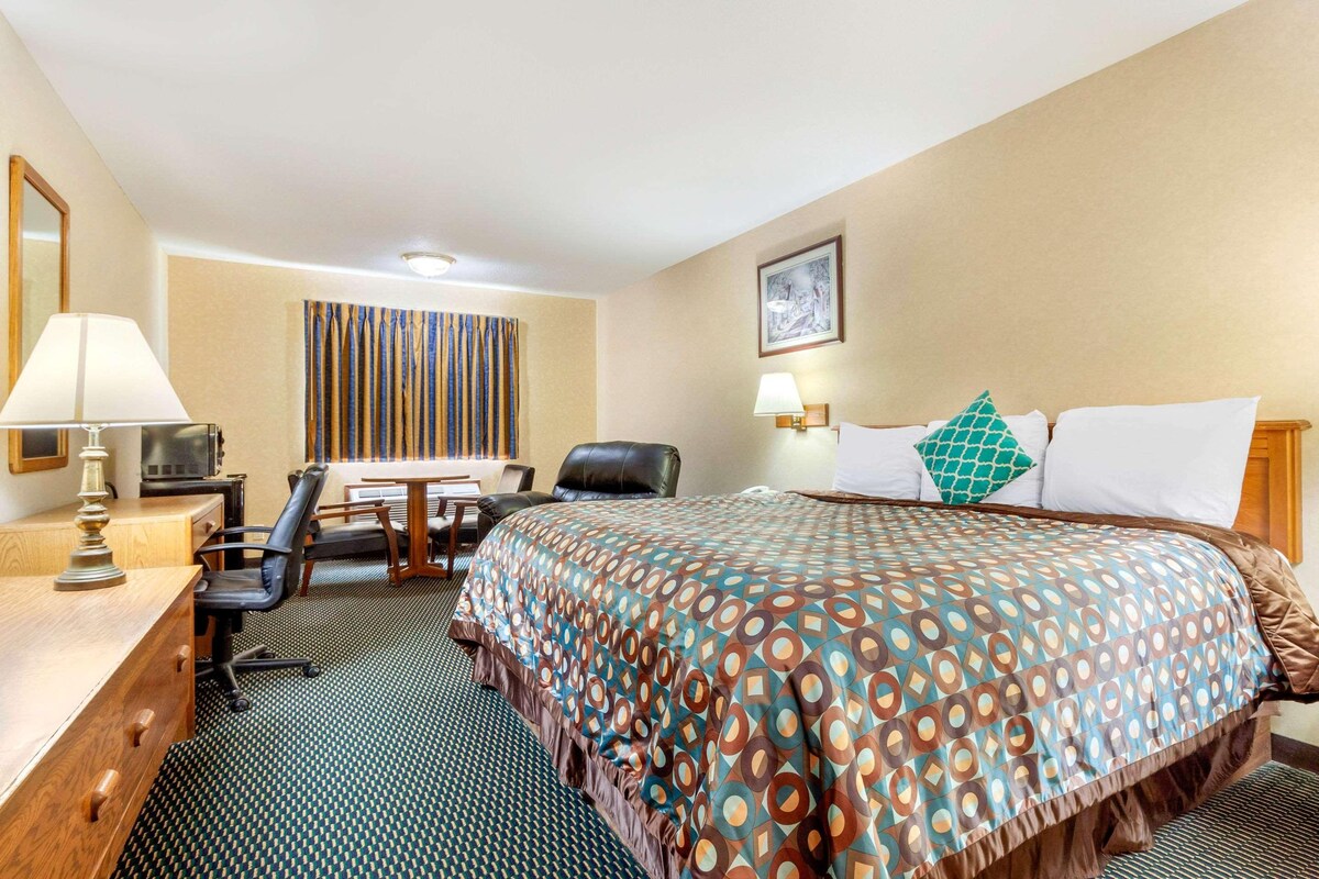 Una habitación de hotel con cama, escritorio, silla y ventana con cortinas a rayas.
