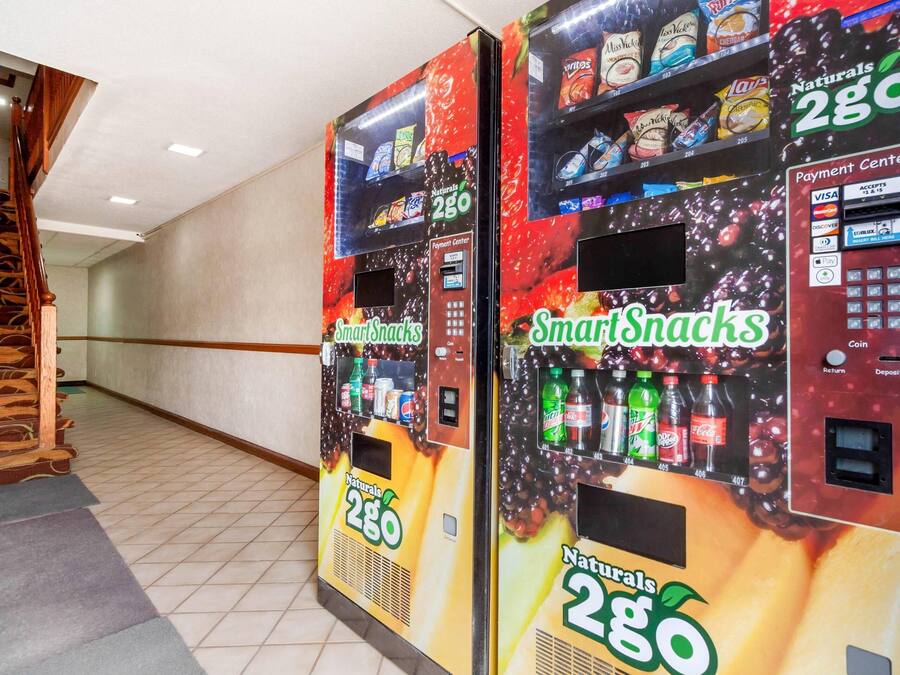 Two vending machines labeled 'SmartSnacks' with a payment center, located in a hallway with a tiled floor and wooden railing.