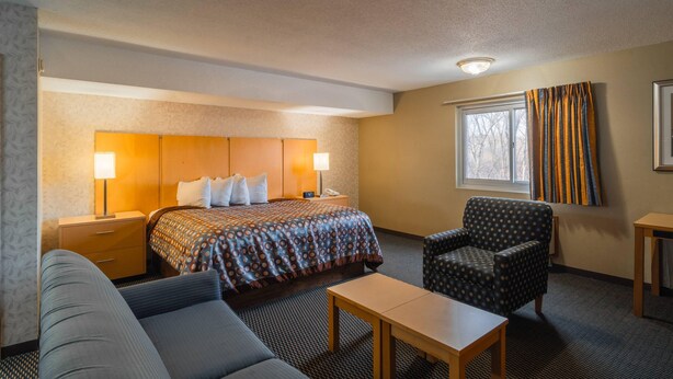 Ein Hotelzimmer mit Bett, Nachttischen, einem Sessel, einem kleinen Tisch und einem Fenster mit Vorhängen.
