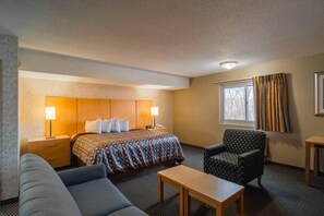 A hotel room with a bed, bedside tables, a chair, a small table, and a window with curtains.