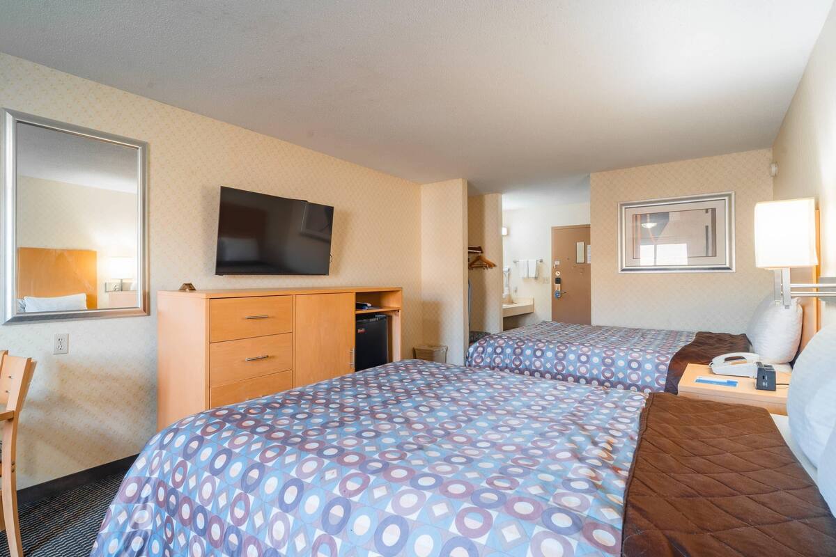 A hotel room with two beds, a TV, a dresser, a mirror, and a lamp.