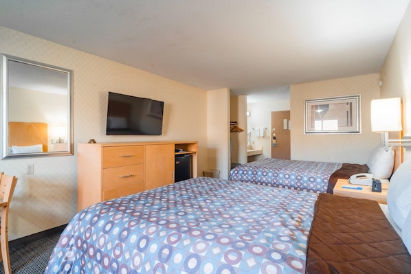 A hotel room with two beds, a TV, a dresser, a mirror, and a lamp. - Rodeway Inn Blair (Blair)