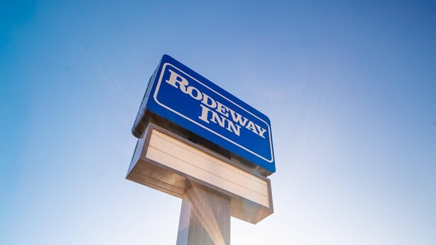 A sign for Rodeway Inn against a clear sky.