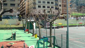 A playground with a basketball court, surrounded by a fence and trees.