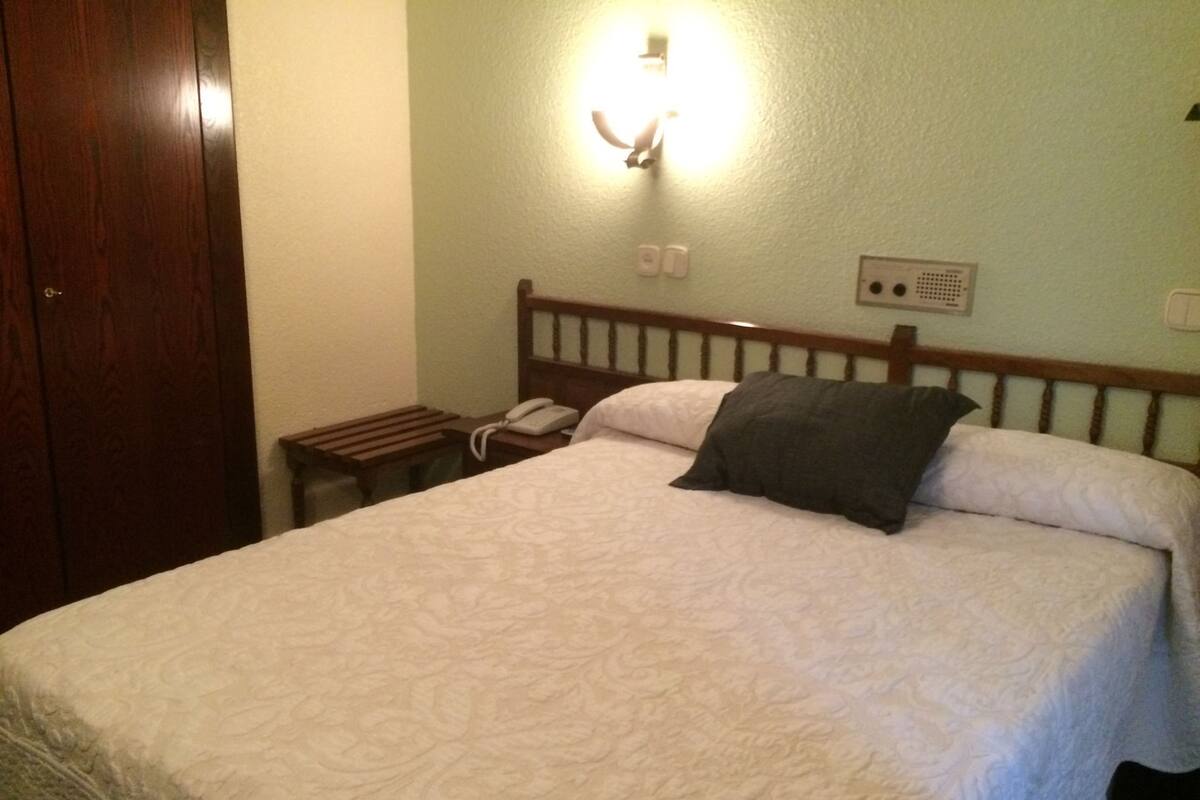 A hotel room with a bed, a bedside table with a lamp, and a telephone.