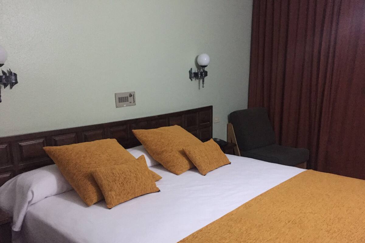 A hotel room with a bed, two pillows, a nightstand, a lamp, and a chair.