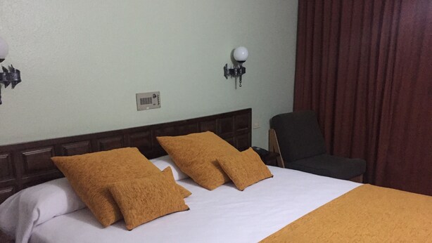 A hotel room with a bed, two pillows, a nightstand, a lamp, and a chair.