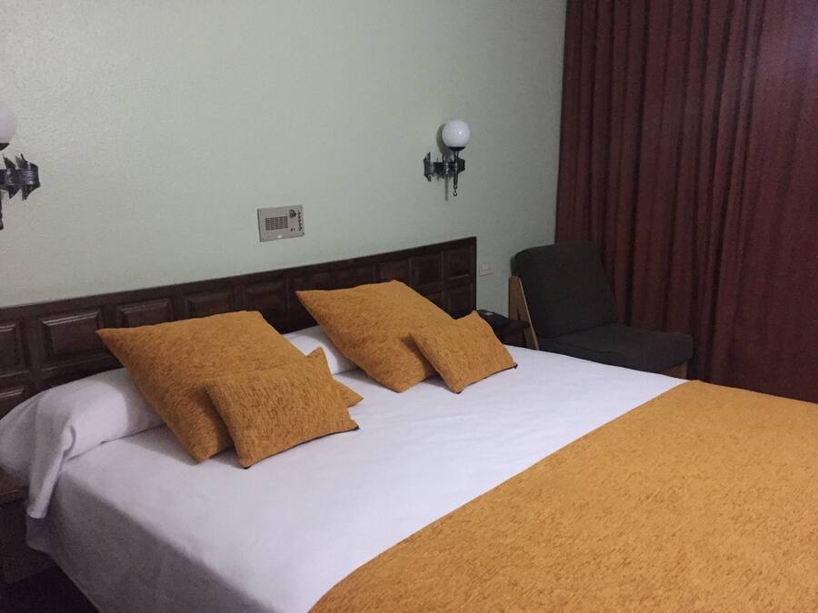 Une chambre d’hôtel avec un lit, deux oreillers, une table de chevet, une lampe et une chaise.
