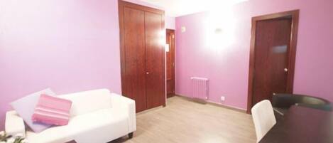 Una habitación con un sofá blanco, una mesita con un control remoto y una mesa de madera oscura.