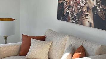 Ein Sofa mit mehreren Kissen in einer neutralen Farbgebung, vor einer Wand mit einem gerahmten Kunstwerk.