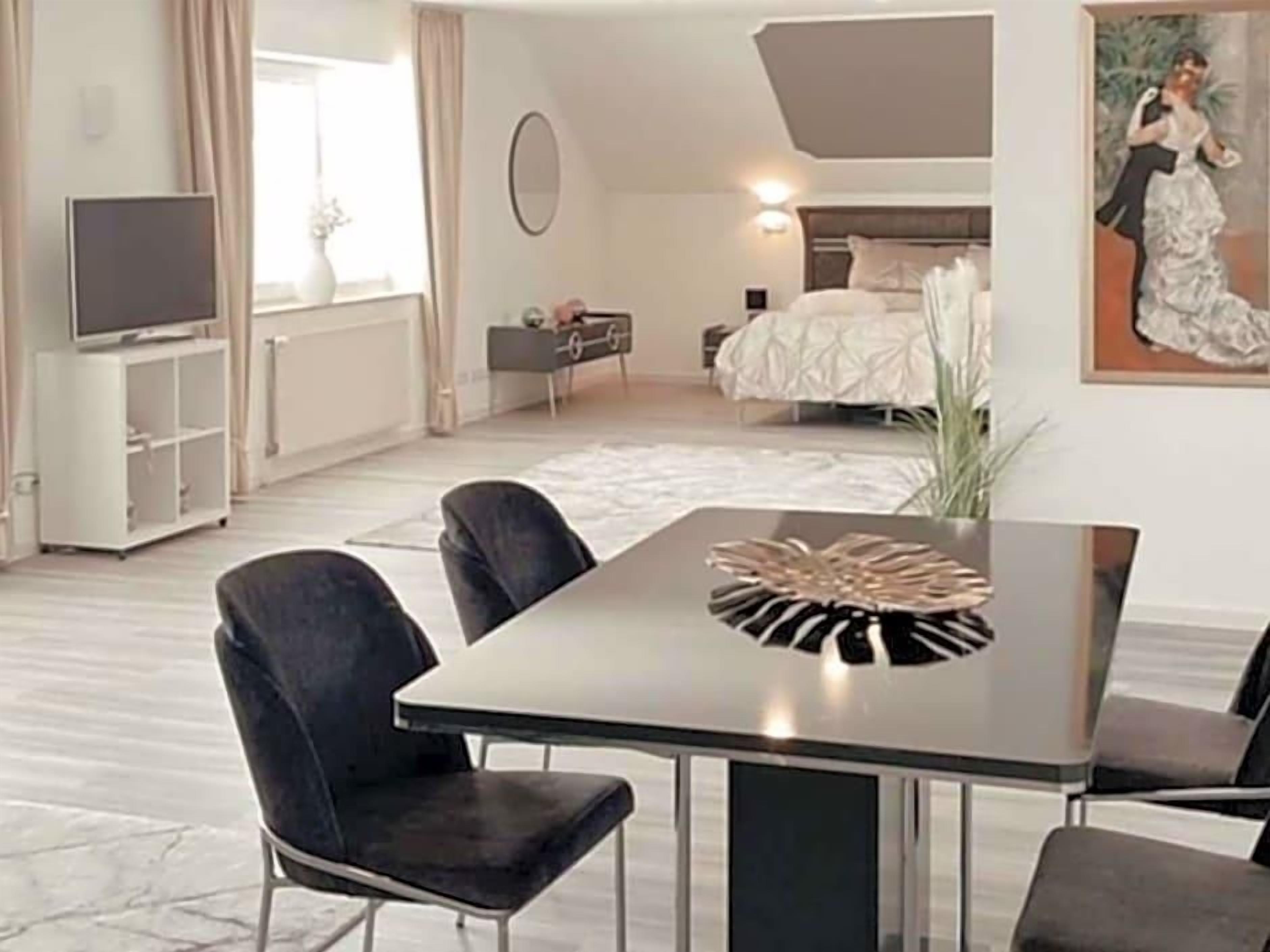 Ein modernes Hotelzimmer mit einem Bett, einem Fernseher, einer Essecke mit Stühlen, einem Tisch und einem Bild an der Wand.