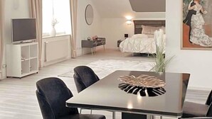 A modern hotel room with a bed, a TV, a dining area with chairs, a table, and a painting on the wall.