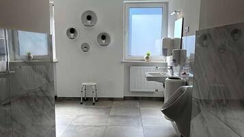 Ein modernes Badezimmer mit Toilette, Waschbecken und einem kleinen Hocker. An den Wänden sind runde Dekorationen und ein Fenster für natürliches Licht vorhanden.
