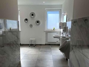 A modern bathroom with a toilet, sink, and a small stool. There are circular wall decorations and a window providing natural light.