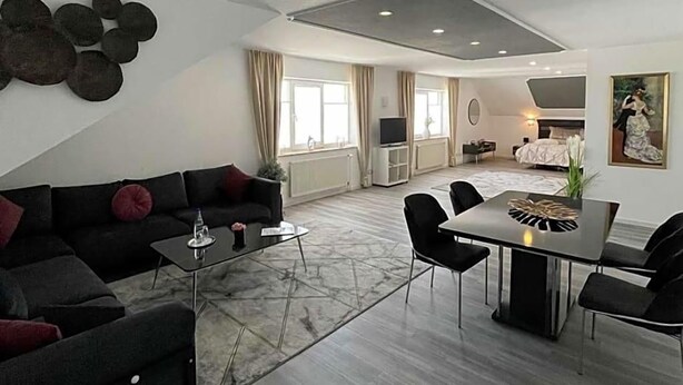A modern living room with a sofa, a dining table, and chairs. There is a flat-screen TV and a painting on the wall.