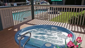 A hot tub on a wooden deck with a pool in the background.