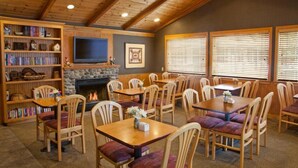 A cozy room with a fireplace, bookshelves, and multiple dining tables and chairs.