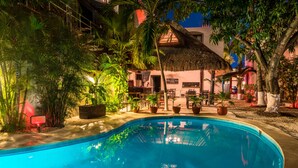 A swimming pool surrounded by potted plants and a building with a thatched roof. - Hotel Hacienda Paradise (Playa del Carmen)
