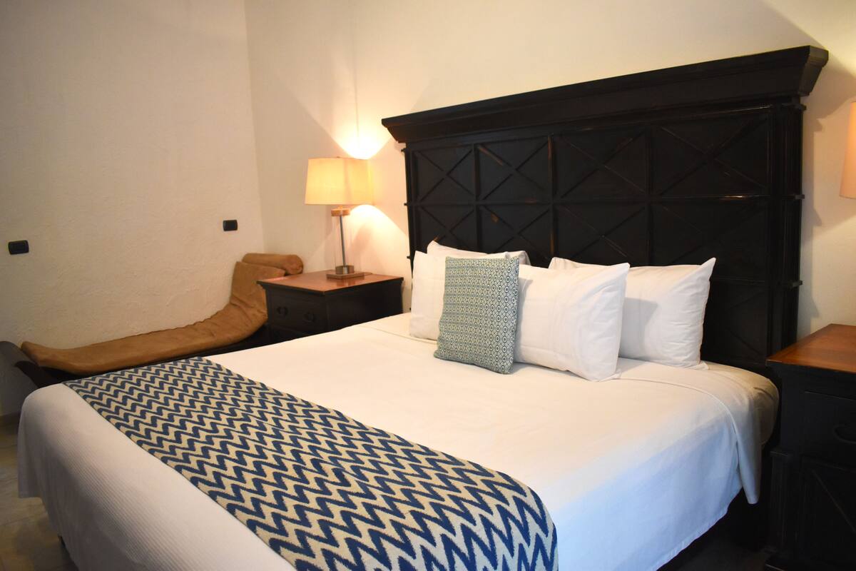 Un lit bien fait, avec une couvre-lit à motifs, une tête de lit au motif géométrique et une lampe de chevet.