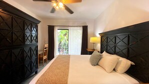 A hotel room with a bed, a ceiling fan, a nightstand with a lamp, a view of the outdoors through a window, and a door leading to a balcony. - Hotel Hacienda Paradise (Playa del Carmen)