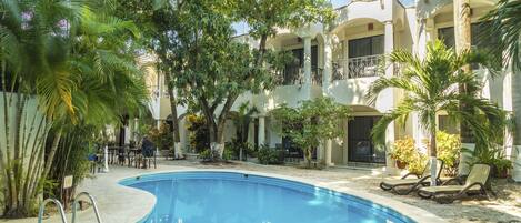 Una piscina rodeada de palmeras y un edificio con balcones.