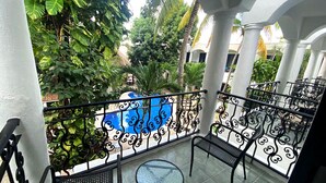 A balcony with a view of a pool, surrounded by lush greenery and white columns. - Hotel Hacienda Paradise (Playa del Carmen)