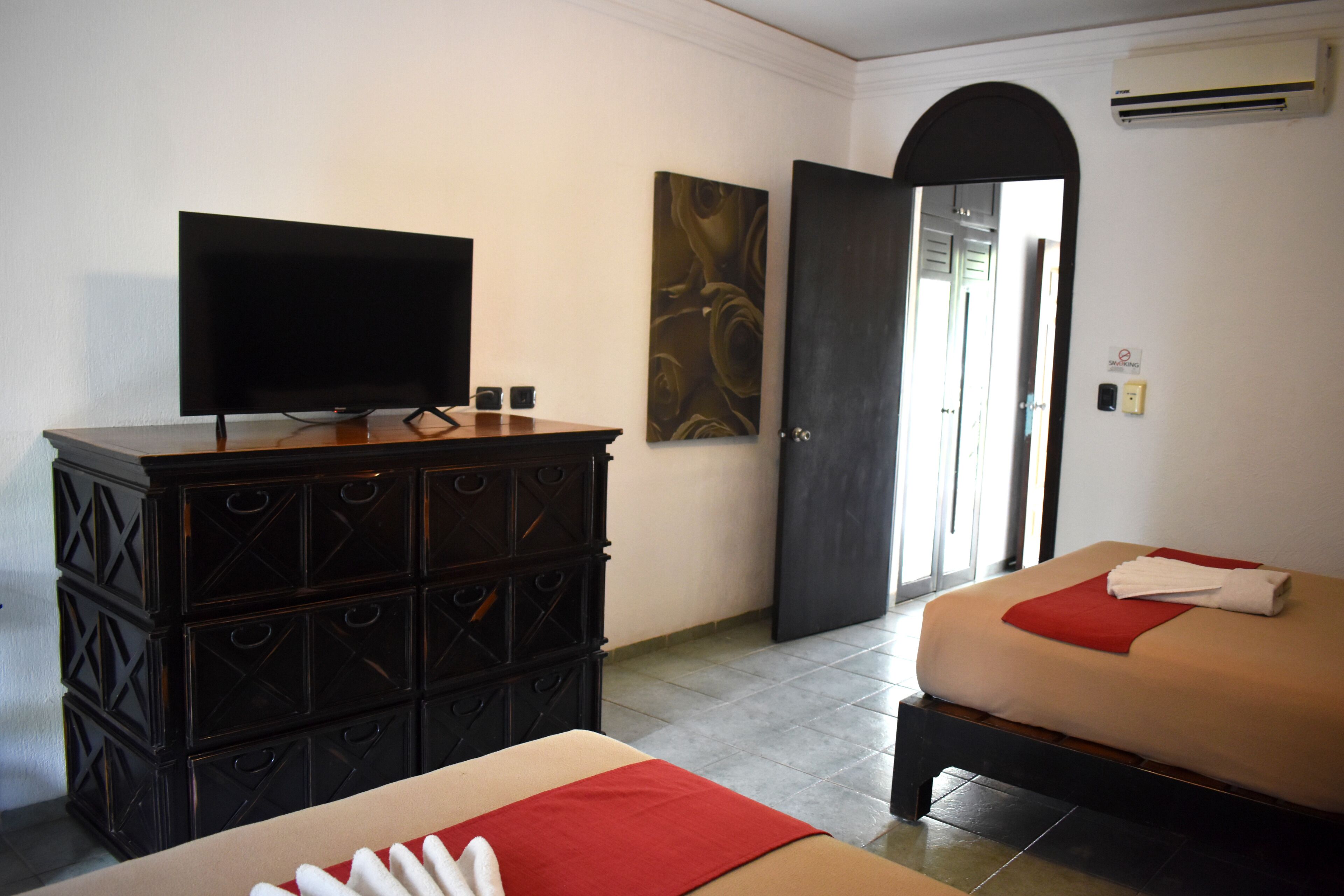 Una habitación de hotel con una cama, un televisor sobre un aparador, una puerta y un aire acondicionado instalado en la pared.