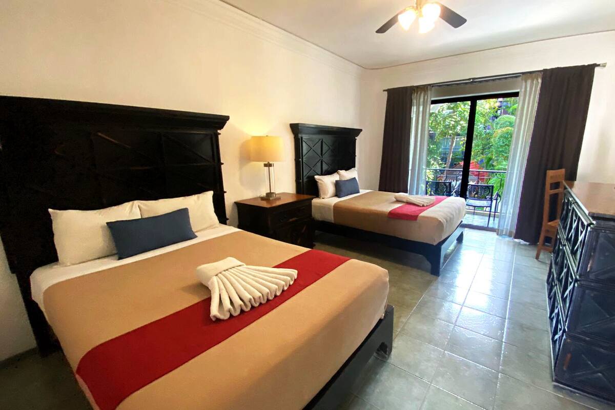 Une chambre d’hôtel avec deux lits, un ventilateur de plafond, un balcon avec vue et un bureau avec une chaise.