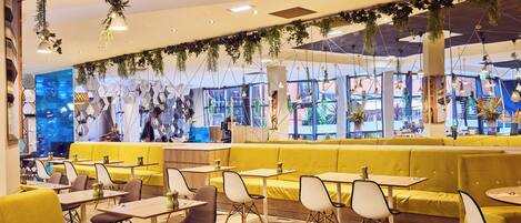 Un intérieur de restaurant moderne avec des sièges jaunes, des tables en bois et des plantes suspendues.