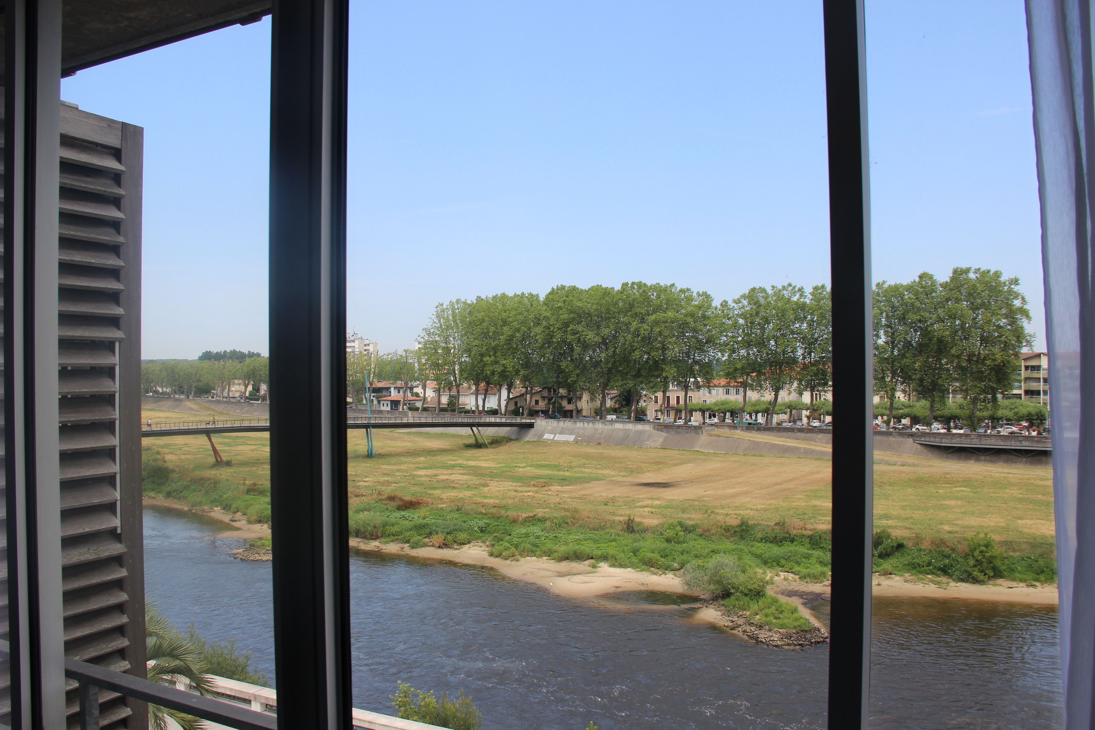 A view of a river with a bridge, trees, and buildings in the background.
