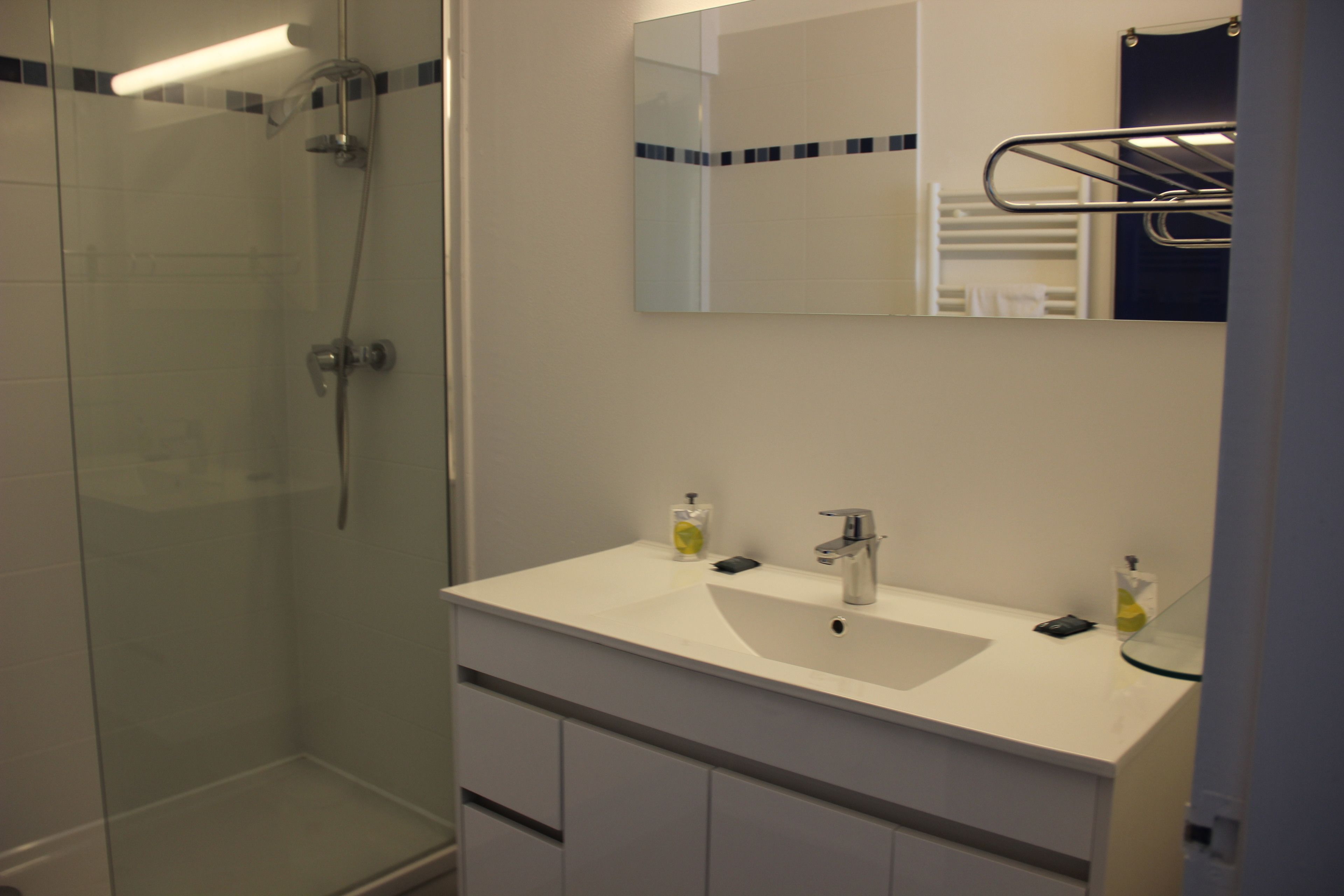 A modern bathroom with a glass-enclosed shower, a white sink with two soap dispensers, and a mirror above the sink.