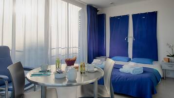A hotel room with a bed, a table with breakfast items, a chair, and a window with curtains.