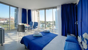 A modern hotel room with a large bed, a balcony with a table and chairs, and a city view.