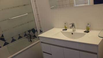 Une salle de bain avec un lavabo blanc, deux distributeurs de savon, un miroir et une cabine de douche en verre.