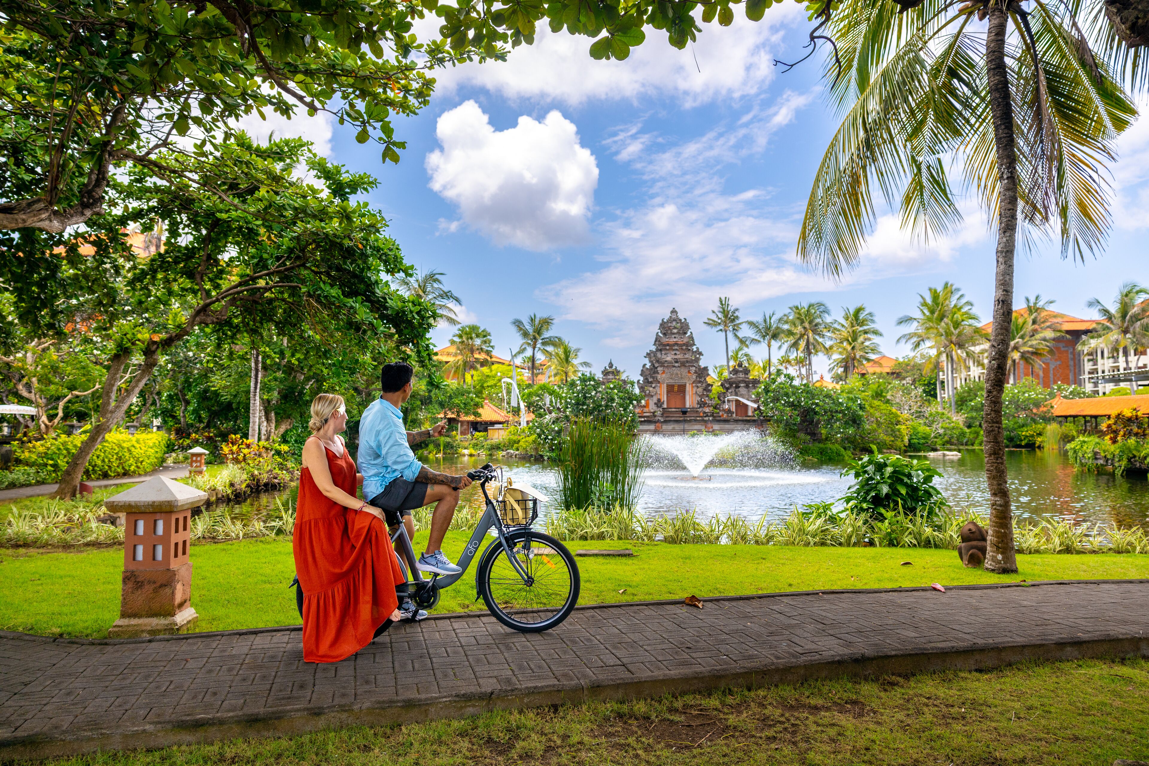 Una pareja en un camino para bicicletas, con un estanque y un templo al fondo.