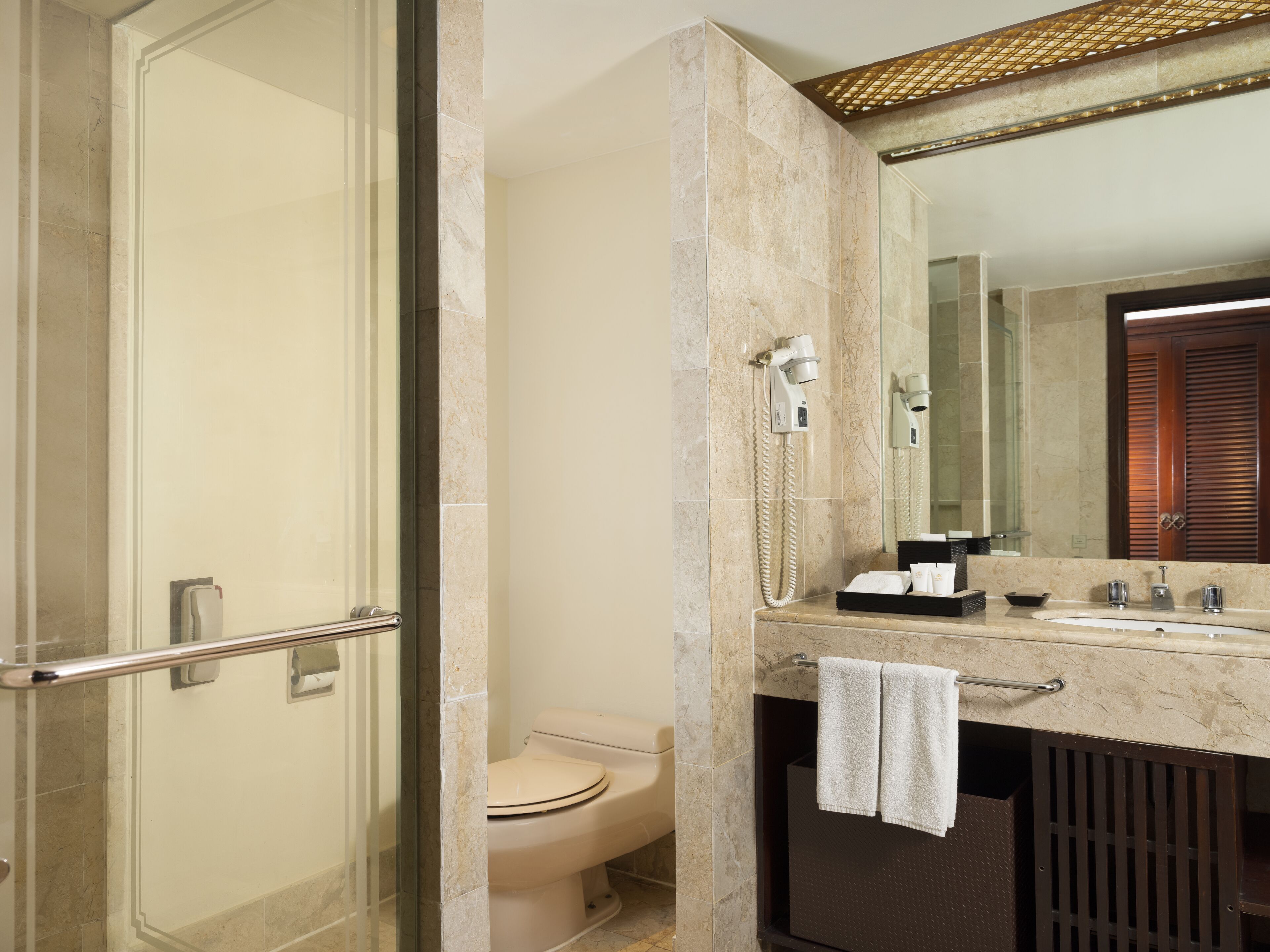 A bathroom with a glass shower enclosure, a toilet, a sink with a towel, and a mirror.