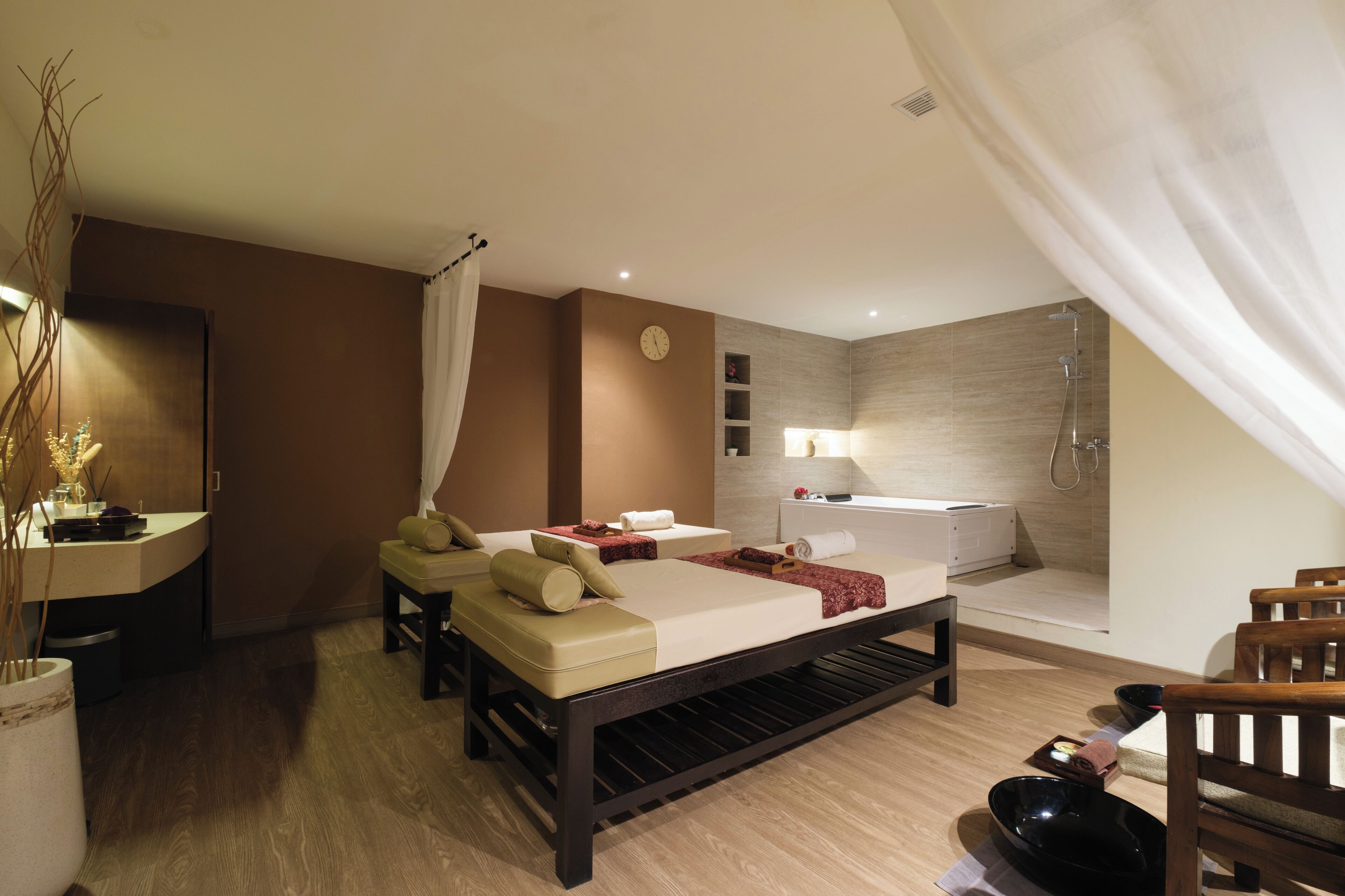 A modern spa room with a bed, a massage table, a bathtub, and a wooden bench.