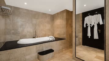 Un baño moderno con una bañera grande, una encimera negra, un espejo y una puerta negra con batas blancas colgadas.