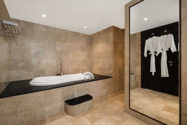 Un bagno moderno con una grande vasca, un piano di lavoro nero, uno specchio e una porta nera con accappatoi bianchi appesi.