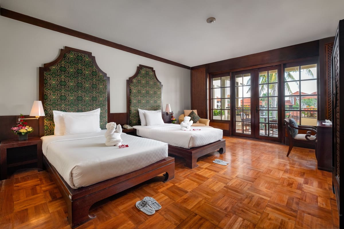 Une chambre d’hôtel avec deux lits, un plancher en bois, de grandes fenêtres et une vue sur l’extérieur.