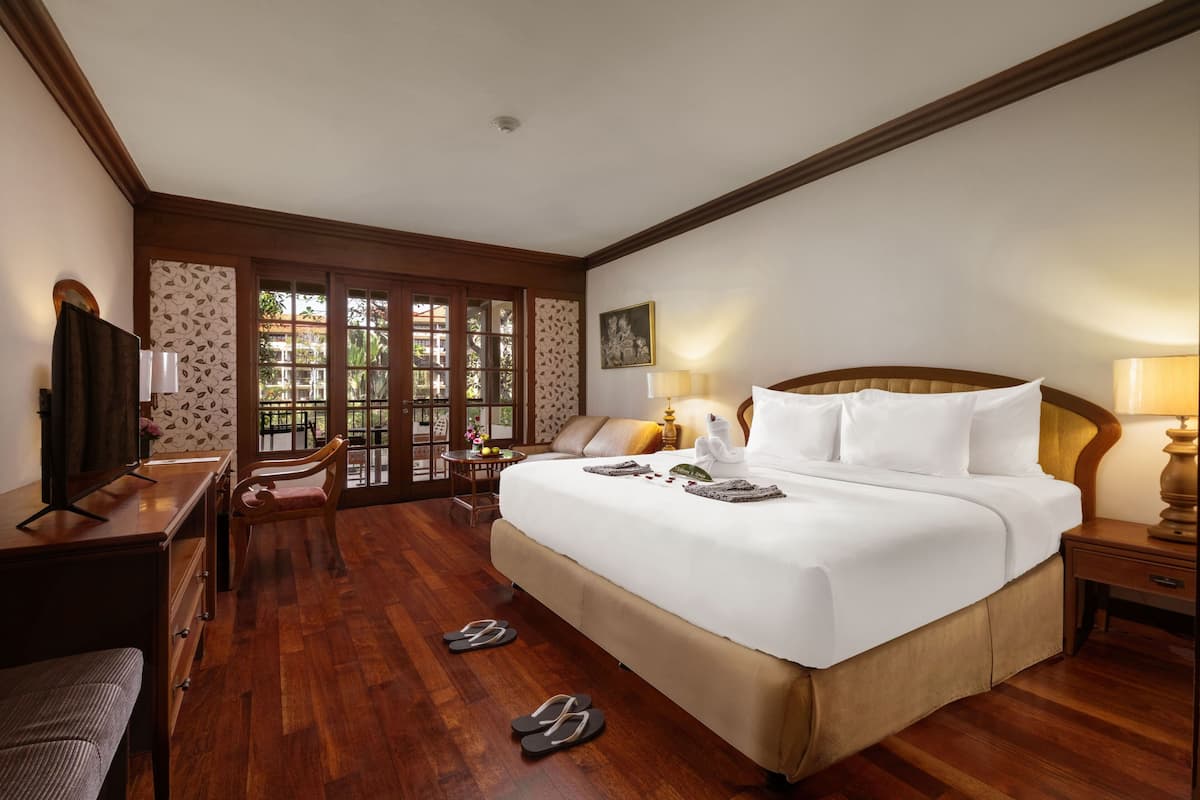 Une chambre d’hôtel avec un grand lit, un plancher en bois, un bureau avec une chaise, une télévision et une fenêtre donnant sur un paysage verdoyant.
