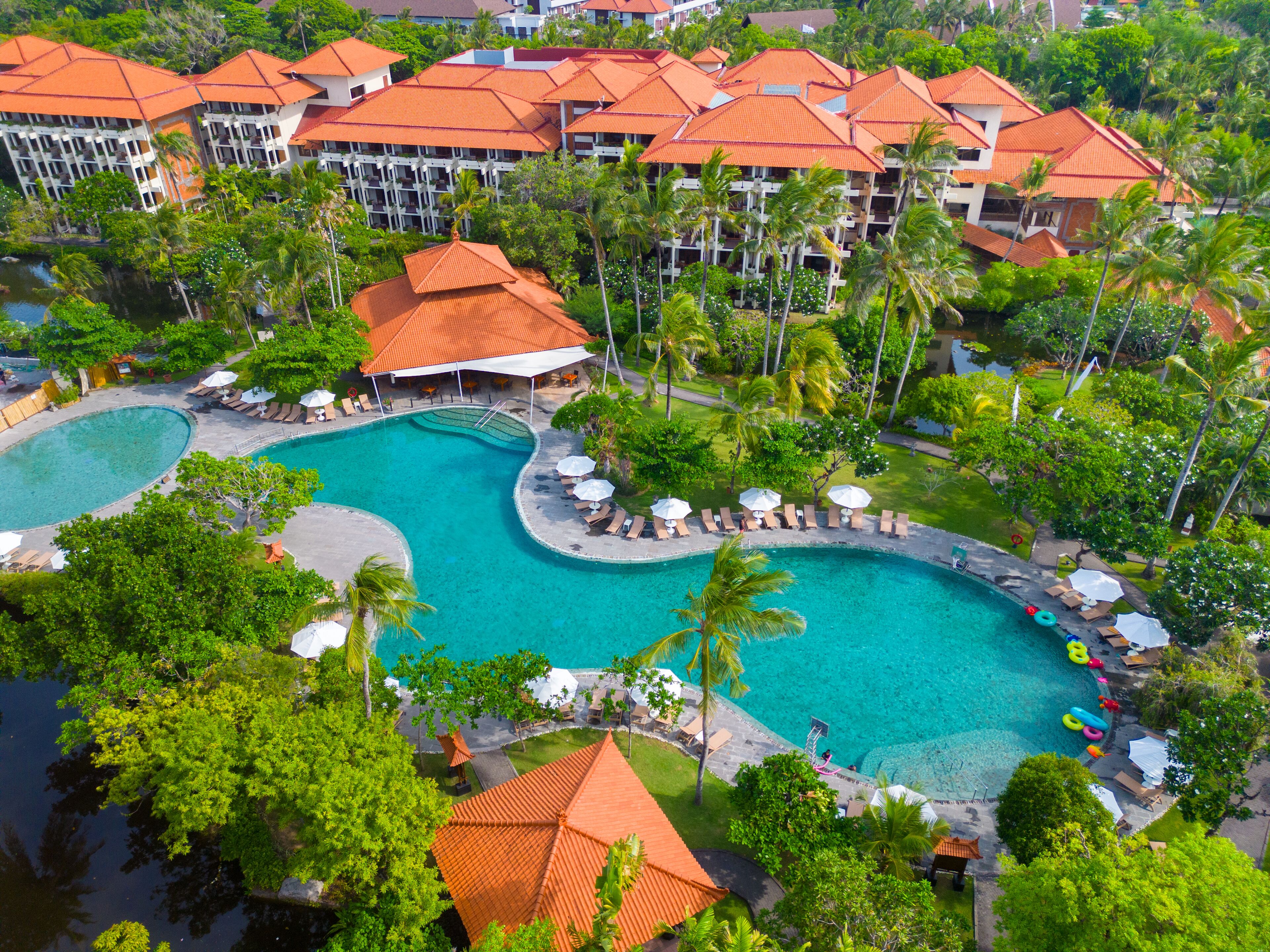 A resort with multiple swimming pools, palm trees, and a large building with red roofs.
