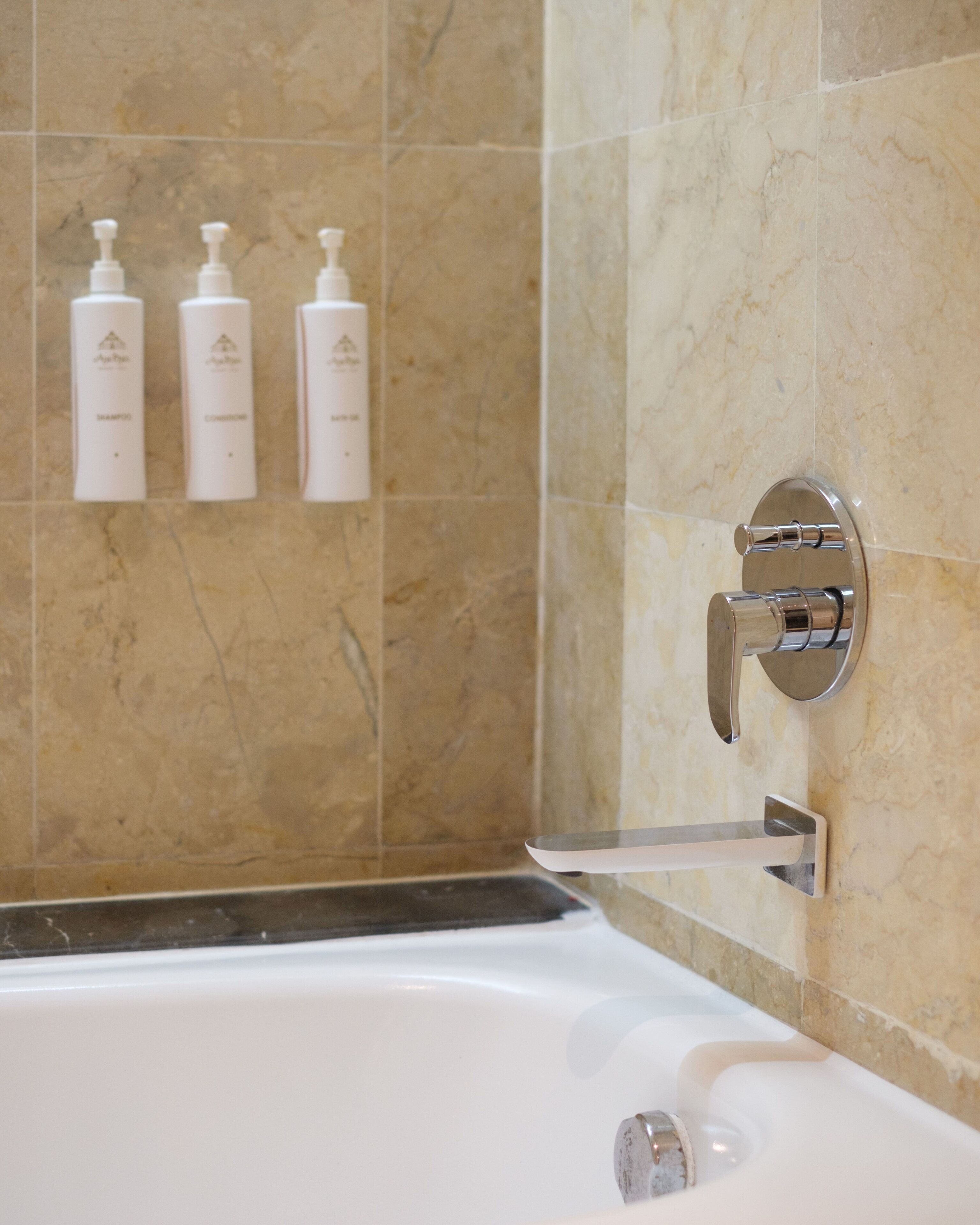 A bathroom with a bathtub, a wall-mounted faucet, and three bottles of toiletries on the wall.