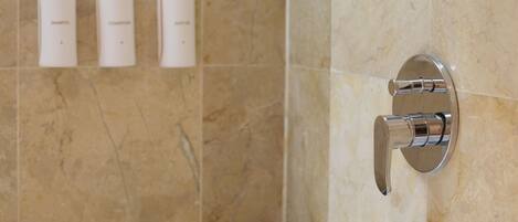 A bathroom with a bathtub, a wall-mounted faucet, and three bottles of toiletries on the wall.