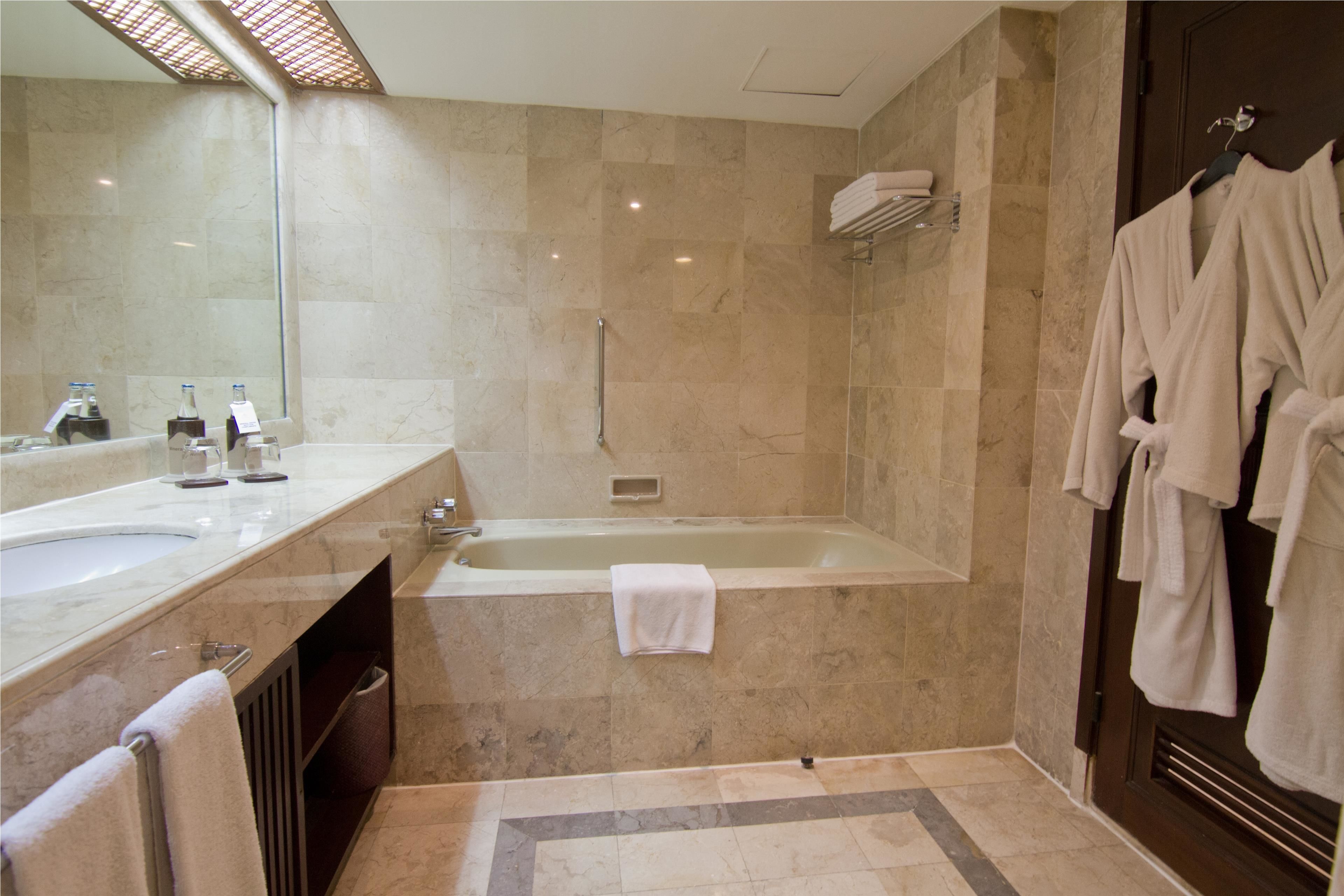 A modern bathroom with a large mirror, two sinks, a bathtub, and a robe rack.