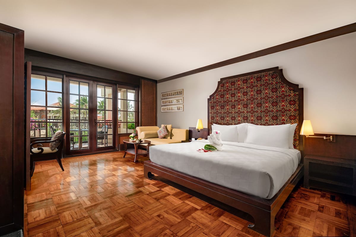 Une chambre d’hôtel avec un grand lit, un canapé, un fauteuil, une table de chevet et une cheminée.