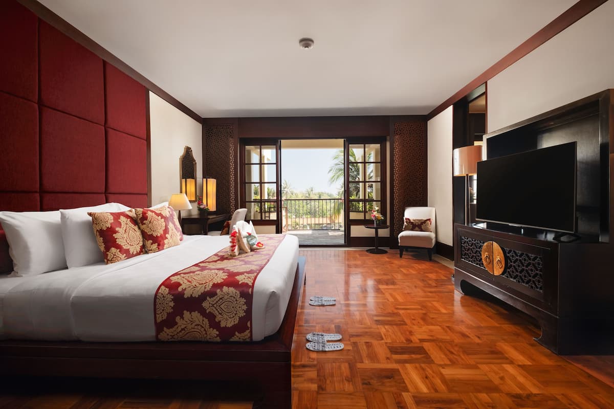 Une chambre d’hôtel avec un grand lit, une télévision et un balcon offrant une vue sur les palmiers.
