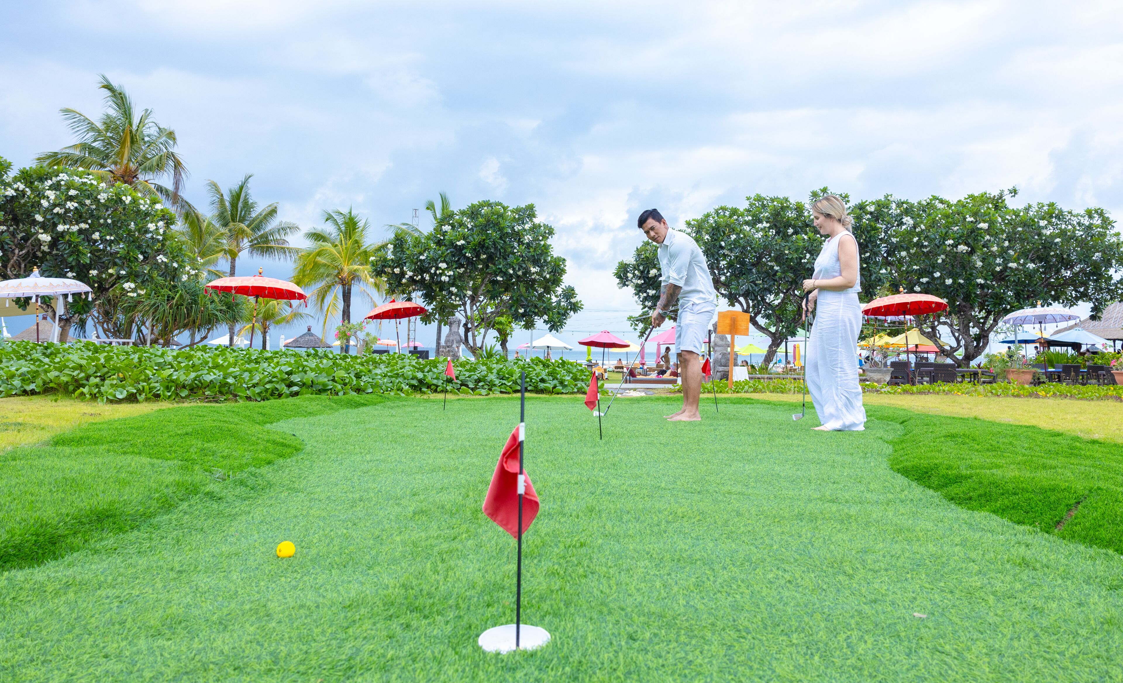 A well-maintained golf course with lush green grass, a putting green, and red flags marking the hole.