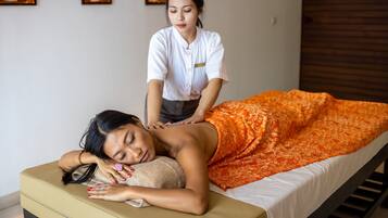 A massage therapy session in a room with a massage table, a person receiving a back massage, and a masseuse standing behind.